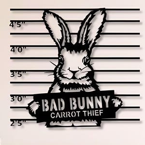 Puede incluir: Arte de pared de metal negro con un conejo sosteniendo un cartel que dice "Bad Bunny Carrot Thief". El conejo está representado en un estilo de foto policial con una tabla de altura en el fondo.
