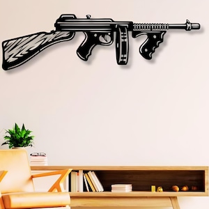 May include: Black metal wall art depicting a stylized machine gun. The gun is mounted on a white wall above a wooden shelf with books and a tan armchair.