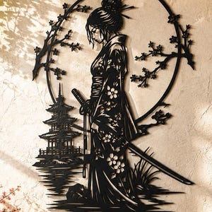 Puede incluir: Una pieza de arte mural de metal negro que muestra la silueta de una persona con kimono sosteniendo una espada, frente a una pagoda y un marco circular de flores de cerezo. El diseño incluye detalles florales y líneas de corte precisas.