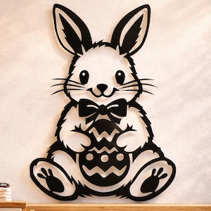 May include: A black and white Easter bunny wall decoration. The bunny is holding an Easter egg and wearing a bow tie. The wall art is made of wood and is a decorative item for the home.