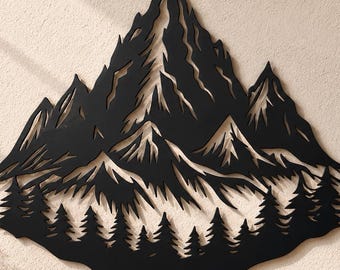 May include: A black metal wall art piece featuring a detailed cutout design of a jagged mountain range with sharp peaks and a dense forest of pine trees at the base. The silhouette is symmetrical and displays intricate lines representing terrain.