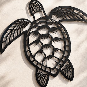 May include: A black metal wall art piece shaped like a sea turtle with a detailed cut-out shell pattern and textured flippers. The design features a symmetrical arrangement of geometric shapes within the shell and intricate markings on the limbs.