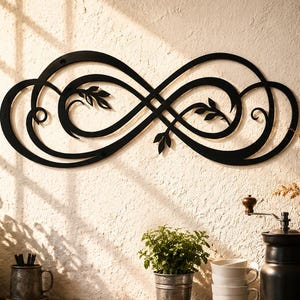 May include: A black metal wall art piece shaped as an infinity symbol with decorative leaf and vine accents. The design features flowing, curved lines that create a continuous loop, mounted on a textured wall surface above a wooden counter.