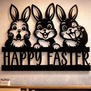 以下が含まれることがあります： 「HAPPY EASTER」の文字と3匹の漫画のウサギが描かれた黒い金属製の壁飾り。ウサギは白い顔と黒い耳をしていて、笑顔です。装飾は明るい色の壁に取り付けられています。