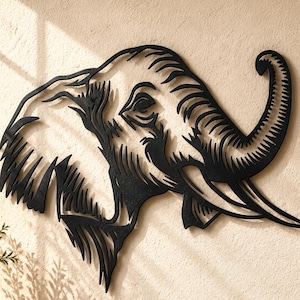 Puede incluir: Una pieza de arte mural de metal negro con forma de cabeza de elefante y recortes estilizados. El diseño presenta una oreja grande, una trompa curvada y un colmillo. La pieza está montada en una pared texturizada sobre una superficie de madera.