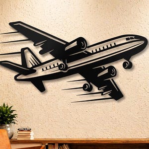 Puede incluir: Arte de pared de avión de metal negro. La pieza decorativa representa un avión en vuelo con líneas de movimiento. La obra de arte está montada en una pared texturizada de color claro. El avión tiene cuatro motores y un diseño detallado.