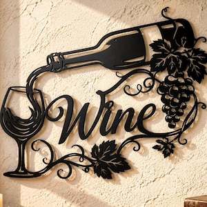 Puede incluir: Una pieza de arte mural de metal negro que muestra una botella de vino vertiendo en una copa, con la palabra Wine en letra cursiva y un racimo de uvas con hojas. El diseño incluye espirales decorativas sobre una pared beige texturizada.