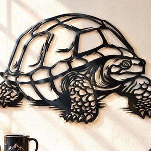 May include: A black metal wall art piece shaped like a tortoise, featuring a detailed cutout design of the shell, head, and legs. The silhouette displays intricate lines and patterns that define the creature's anatomy in a flat, dark finish.