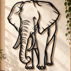 May include: A black metal wall art piece shaped like an elephant silhouette. The design features clean, bold lines outlining the elephant's large ears, trunk, and tusks, creating a minimalist representation of the animal mounted on a textured wall.