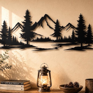 May include: A black metal wall art piece featuring a silhouette of a mountain range, a dense forest of pine trees, and a reflective lake. The design is elongated and horizontal, showcasing sharp peaks and detailed tree outlines in a flat finish.