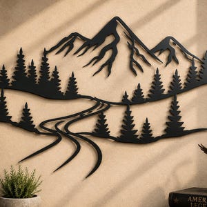 Pode incluir: Uma peça de arte de parede em metal preto apresentando a silhueta de uma cordilheira com picos irregulares, uma densa floresta de pinheiros e um caminho de rio sinuoso que flui pela paisagem. O design é plano, intrincado e monocromático.