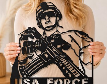 May include: Black metal wall art depicting a soldier holding a rifle. The artwork features the words "USA FORCE" at the bottom. The soldier is wearing a helmet and sunglasses. The piece is cut from a single sheet of metal.