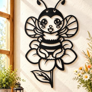 May include: A black metal wall art piece featuring a stylized bee with large eyes and antennae, resting on a flower with a single leaf. The design is flat, cut from a single sheet of material, and displays a symmetrical, cartoon-like insect.