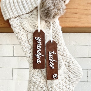 Peut inclure: Deux étiquettes de chaussette de Noël en bois avec des lettres blanches. Une étiquette dit "Grandpa" et l'autre dit "Tucker" avec une empreinte de patte.