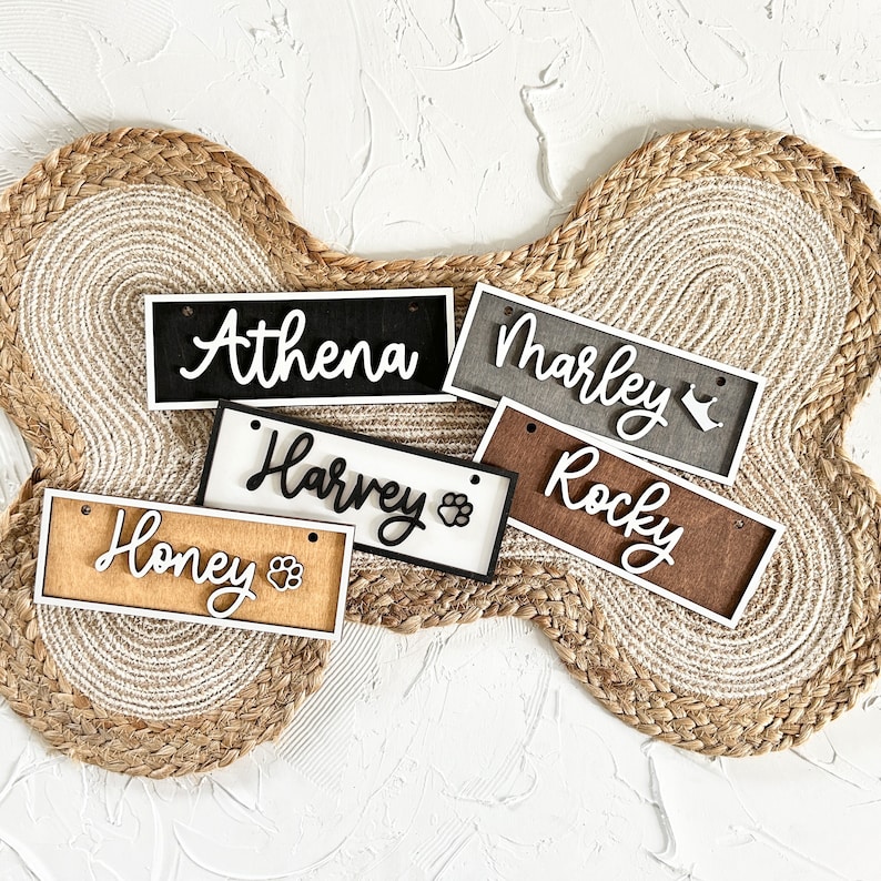 K&ouml;nnte beinhalten: F&uuml;nf h&ouml;lzerne Hundename-Tags mit Pfotenabdr&uuml;cken. Die Namen sind "Athena", "Marley", "Harvey", "Rocky" und "Honey".