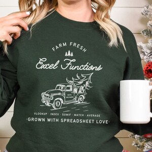 May include: Dark green sweatshirt with white text: "FARM FRESH Excel Functions" above a vintage truck carrying a Christmas tree. Below the truck are the words "VLOOKUP INDEX SUMIF MATCH AVERAGE" and "GROWN WITH SPREADSHEET LOVE."