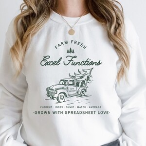 May include: White sweatshirt with a green graphic. The graphic features a vintage truck carrying a Christmas tree, with the text "FARM FRESH Excel Functions" and spreadsheet-related terms. The phrase "GROWN WITH SPREADSHEET LOVE" is also included.