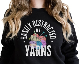 May include: Black sweatshirt with the text "Easily Distracted by Yarns" in white lettering. A colorful illustration of yarn balls and knitting needles is in the center of the text.