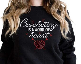 May include: Black sweatshirt with the text "Crocheting is a work of heart" in white with a red heart and yarn graphic.