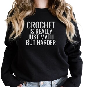 May include: Black sweatshirt with white text that reads "Crochet is really just math but harder".