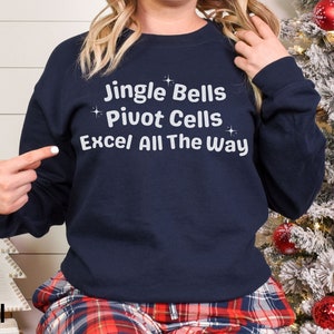 May include: Navy blue sweatshirt with the text "Jingle Bells Pivot Cells Excel All The Way" in white. The sweatshirt is part of a holiday-themed collection. The text is in a playful font, and the design includes small star accents.