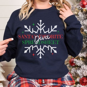 Könnte beinhalten: Marineblaues Sweatshirt mit weißem Schneeflocken-Design und dem Text "SANTA'S FAVORITE SPREADSHEET" in Rot und Grün. Ein festliches Weihnachts-Kleidungsstück.