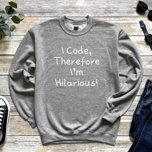 K&ouml;nnte beinhalten: Grauer Pullover mit dem Aufdruck "I Code, Therefore I'm Hilarious!" in Wei&szlig;.
