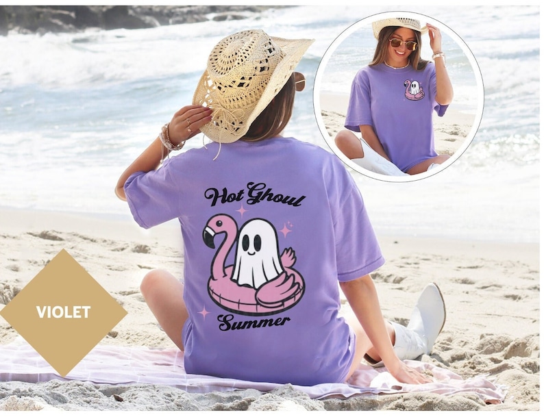 May include: A violet t-shirt featuring a ghost on a pink flamingo floatie, with the words "Hot Ghoul Summer". The shirt is worn on a beach with the sea in the background. A smaller image shows the front of the shirt.