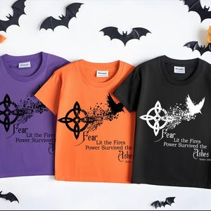 May include: Three short-sleeved t-shirts in purple, orange, and black, each featuring a Celtic knot design with the text "Fear, Lit the Fires, Power Survived the Ashes." Halloween-themed with bat and leaf decorations.