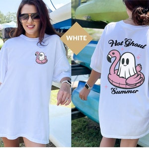 May include: White t-shirt with a cartoon ghost on a pink flamingo float. The back of the shirt has the words "Hot Ghoul Summer" above the ghost and flamingo design. A fun summer themed top.