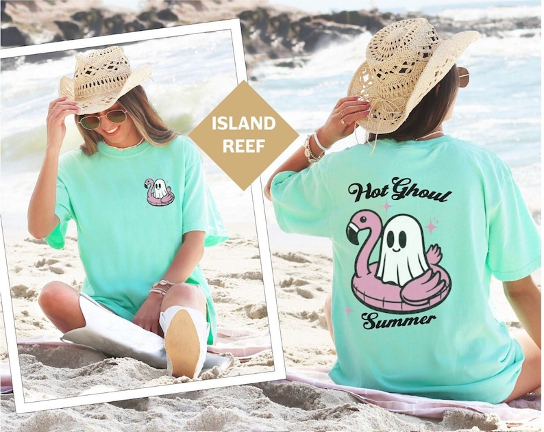 May include: A pale green t-shirt featuring a ghost on a pink flamingo inflatable. The back of the shirt says "Hot Ghoul Summer" with a ghost on a flamingo floatie. The shirt is part of the "Island Reef" collection.