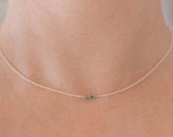 May include: A delicate silver necklace with a fine chain. The necklace features a small cluster of turquoise-coloured beads centered on the chain. The necklace is shown against a skin tone background.