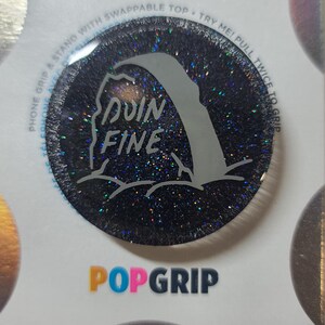 May include: A black PopGrip with a glittery finish and the words "DOIN FINE" in white. The design includes a stylized wave graphic. The PopGrip is round and has a swappable top.