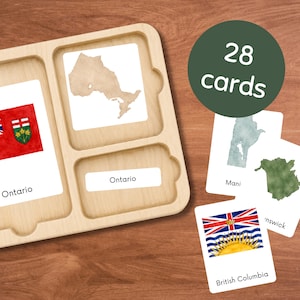May include: A light-coloured wooden tray with three rectangular compartments, holding white cards featuring maps and flags of Canadian provinces. One card shows the Ontario flag and text, another a map of Ontario, and others show regional maps and flags.