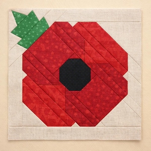 May include: A square fabric quilt block featuring a stylized red poppy flower with a black octagonal center and a green leaf at the top left corner. The poppy is constructed from various shades of red fabric pieces set against a light beige background.