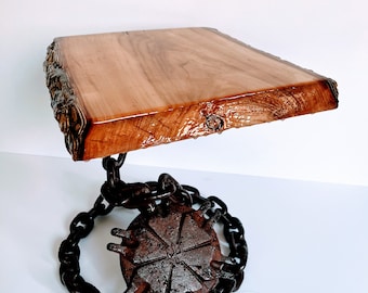 May include: A wooden table top with live edge details sits on a metal base with a chain and a circular gear design.