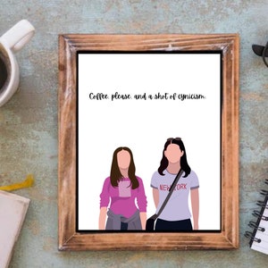 May include: A framed print with a white background and a quote that reads "Coffee, please and a shot of cynicism." Two cartoon women are depicted in the print, one wearing a pink shirt and the other wearing a light blue shirt with the words "New York" printed on it.