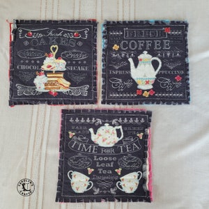 May include: Three square fabric coasters with decorative stitching and text. One says "Fresh Cakes" with images of desserts. Another says "Fresh Coffee" with a teapot graphic. The third says "Time for Tea" with teacups and a teapot.
