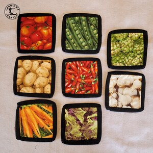 May include: Nine square fabric coasters with black borders, each displaying a different vegetable print: tomatoes, green beans, artichokes, potatoes, red peppers, garlic, carrots, and lettuce. The coasters are arranged in a grid.