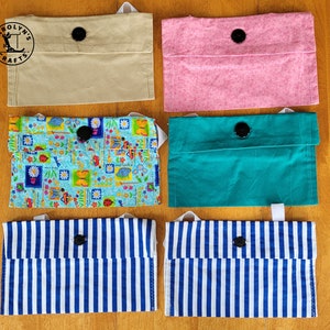 May include: A selection of fabric pouches in different colours and patterns. The pouches include solid beige, pink, and teal, alongside patterned options with a floral and a blue and white striped design. Each pouch has a black button closure.