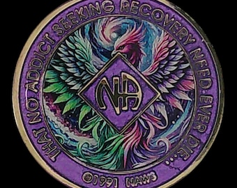 May include: A round purple metal medallion featuring a central diamond shape with the letters NA. A colorful phoenix illustration surrounds the center. The outer border text reads THAT NO ADDICT SEEKING RECOVERY NEED EVER DIE and 1991 NAWS.