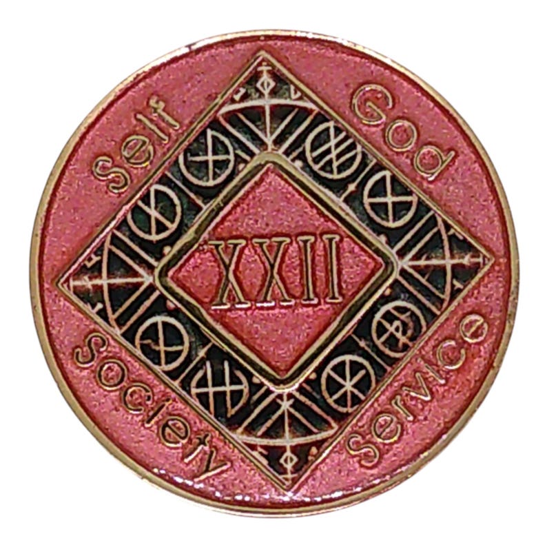 May include: A round pink and gold metal medallion featuring a central diamond shape with the Roman numeral XXII inside. The words Self, God, Society, and Service are embossed around the perimeter, with black accents filling the geometric patterns.