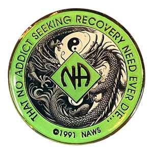 Könnte beinhalten: Eine runde, grün-goldene Münze mit dem Text "THAT NO ADDICT SEEKING RECOVERY NEED EVER DIE..." und "©1991 NAWS". In der Mitte befindet sich eine grüne Raute mit "NA" und zwei Drachen.
