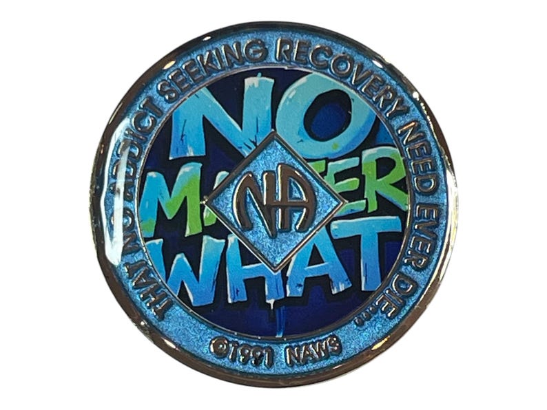Blue and green Narcotics Anonymous medallion with graffiti-style text reading ‘No Matter What’ around the NA symbol, bordered by the phrase ‘That no addict seeking recovery need ever die.’