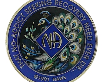 May include: A circular blue and gold metal medallion featuring a peacock illustration and a central diamond shape with the letters NA. The border text reads THAT NO ADDICT SEEKING RECOVERY NEED EVER DIE, with 1991 NAWS printed at the bottom.