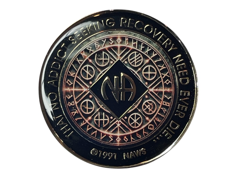 Narcotics Anonymous recovery medallion featuring Norse rune-inspired symbols and circular geometric patterns in metallic bronze and black. The NA logo sits at the center, surrounded by the quote “That No Addict Seeking Recovery Need Ever Die,” symbolizing strength, resilience, and spiritual protection in recovery.