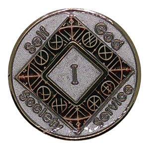 May include: A circular silver-toned metal medallion featuring a central diamond shape with the Roman numeral I inside. The text Self, God, and Society Service is embossed around the perimeter. The design includes intricate geometric line patterns.