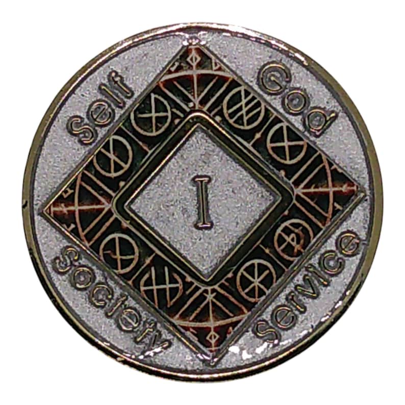 May include: A circular silver-toned metal medallion featuring a central diamond shape with the Roman numeral I inside. The text Self, God, and Society Service is embossed around the perimeter. The design includes intricate geometric line patterns.