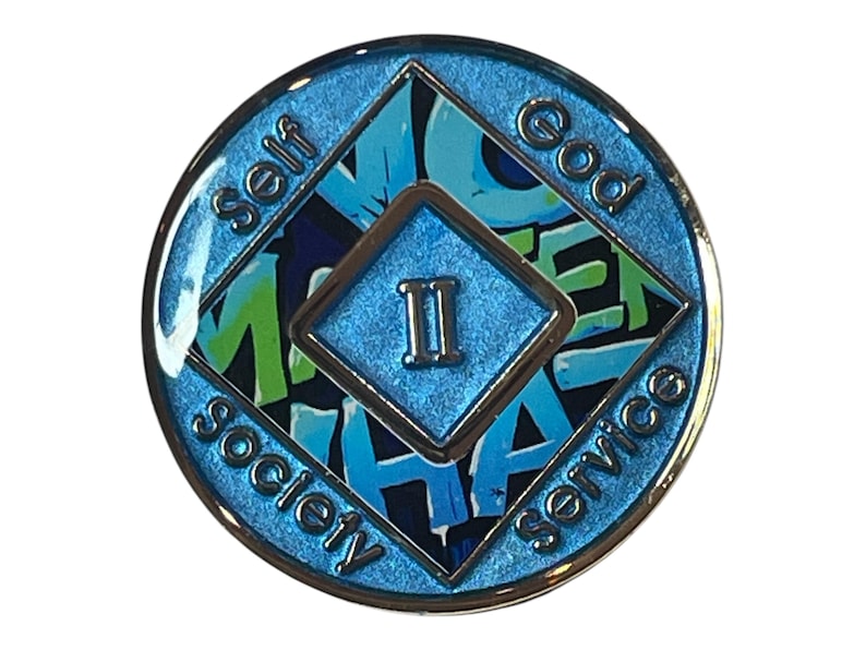 Blue Narcotics Anonymous recovery medallion with a diamond center showing the Roman numeral II. Surrounding words read ‘Self,’ ‘God,’ ‘Society,’ and ‘Service,’ with graffiti-style text ‘No Matter What’ in the background.