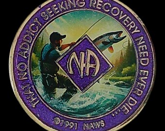 May include: A round purple and gold medallion featuring a fisherman in a river with a jumping fish. The center has a purple diamond with the letters NA. The border text reads THAT NO ADDICT SEEKING RECOVERY NEED EVER DIE and 1991 NAWS.